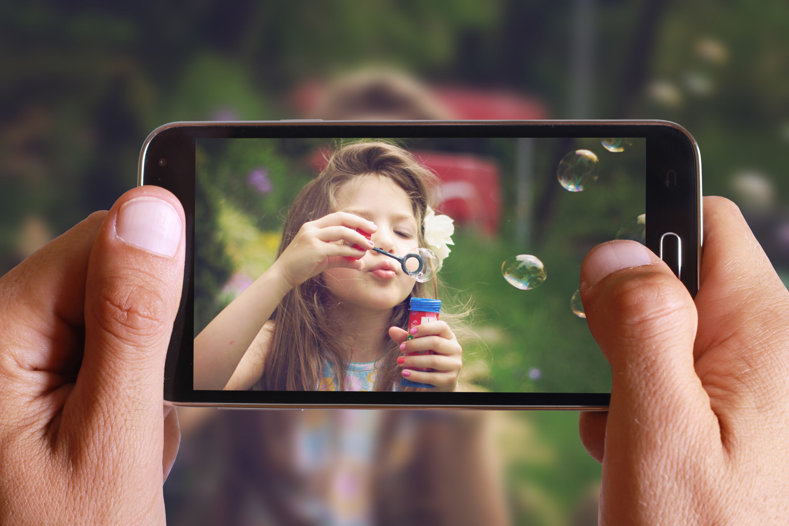 Male hand taking photo of Vintage Portrait of beautiful girl blowing bubbles with cell, mobile phone. Kids, childhood, family concept.