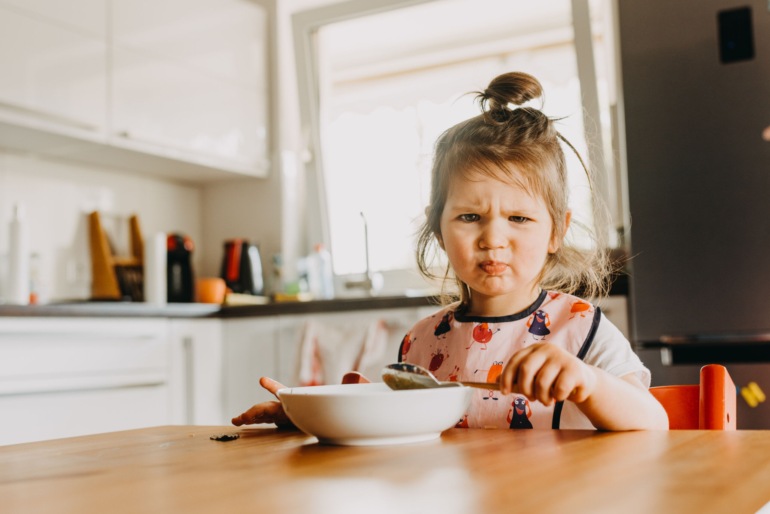 adorable funny toddler girl looks unhappy with her meal